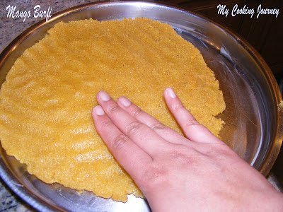 Pressing down and spreading the Mango Burfi mixture in the tray