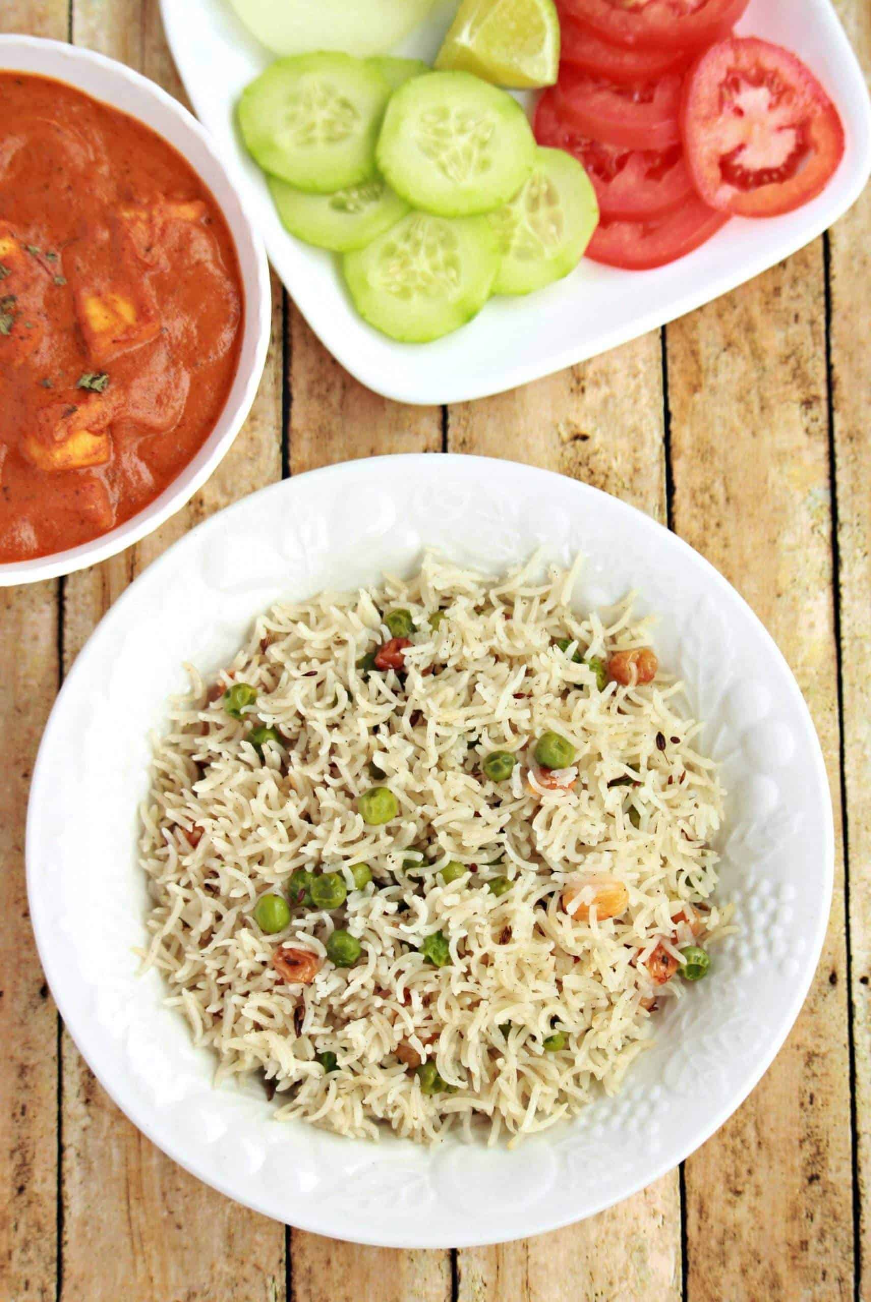 peas pulao in a white bowl with curry and salad on side