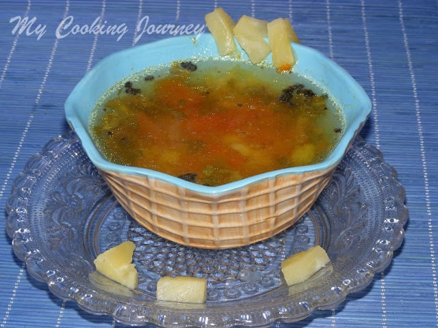 Pineapple rasam in a Bowl with some pineapple pieces 