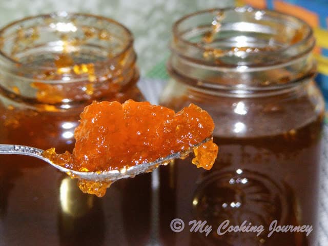 Jalapeno Jelly scooped in a spoon with 2 jars of jelly in the background