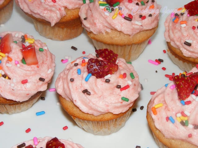Cupcakes with Strawberry frosting on it and also some chopped strawberry.
