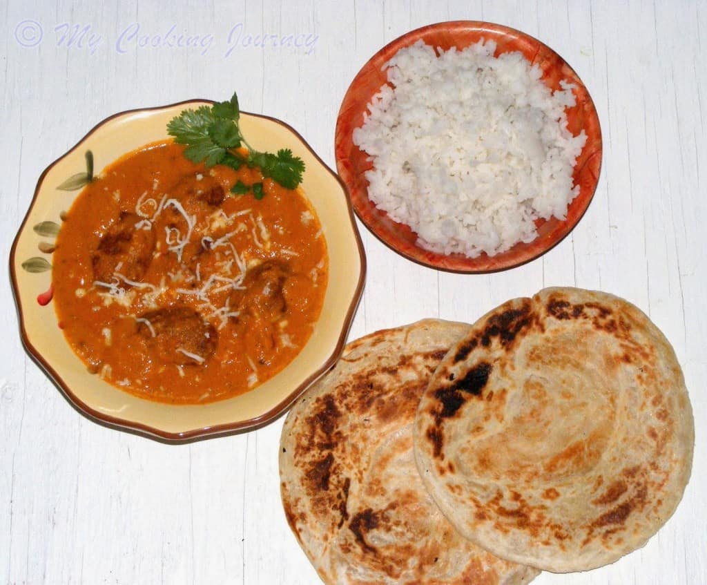 Malai Kofta in a bowl with garnish and rice and parathas on the side