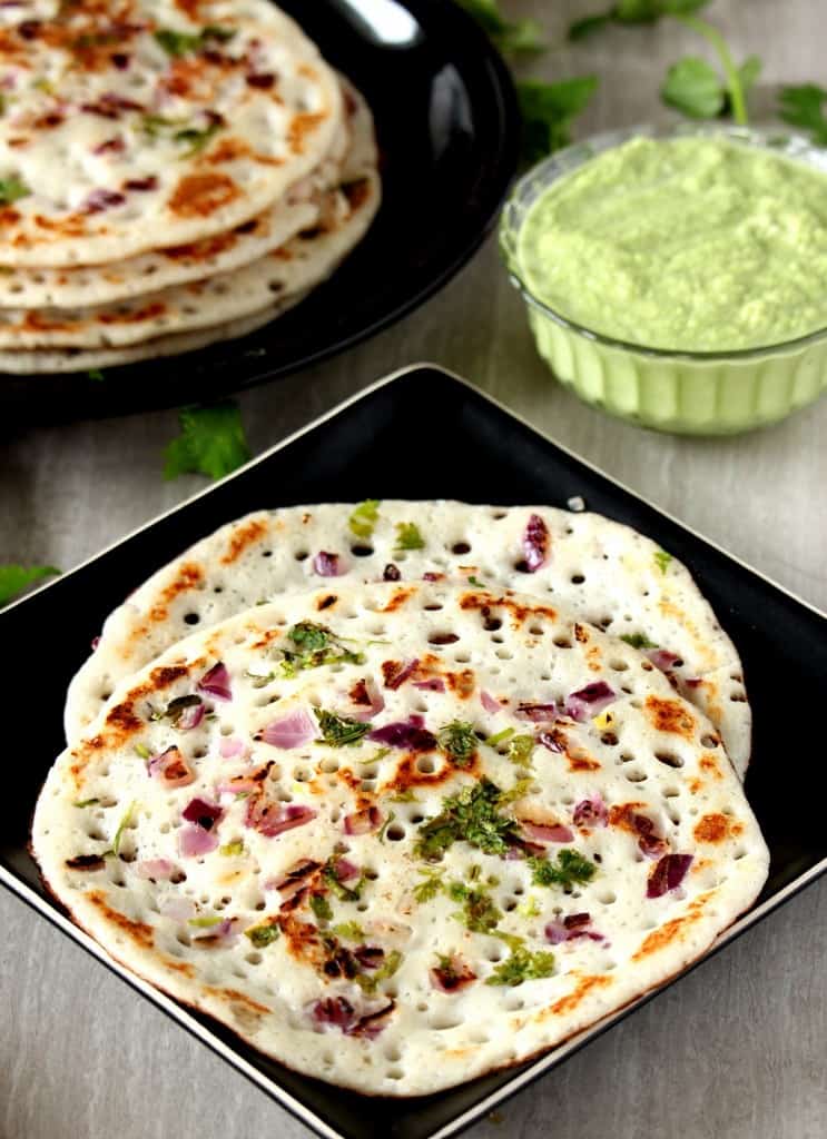 Onion Oothappam stacked in two different plates with chutney on the side.