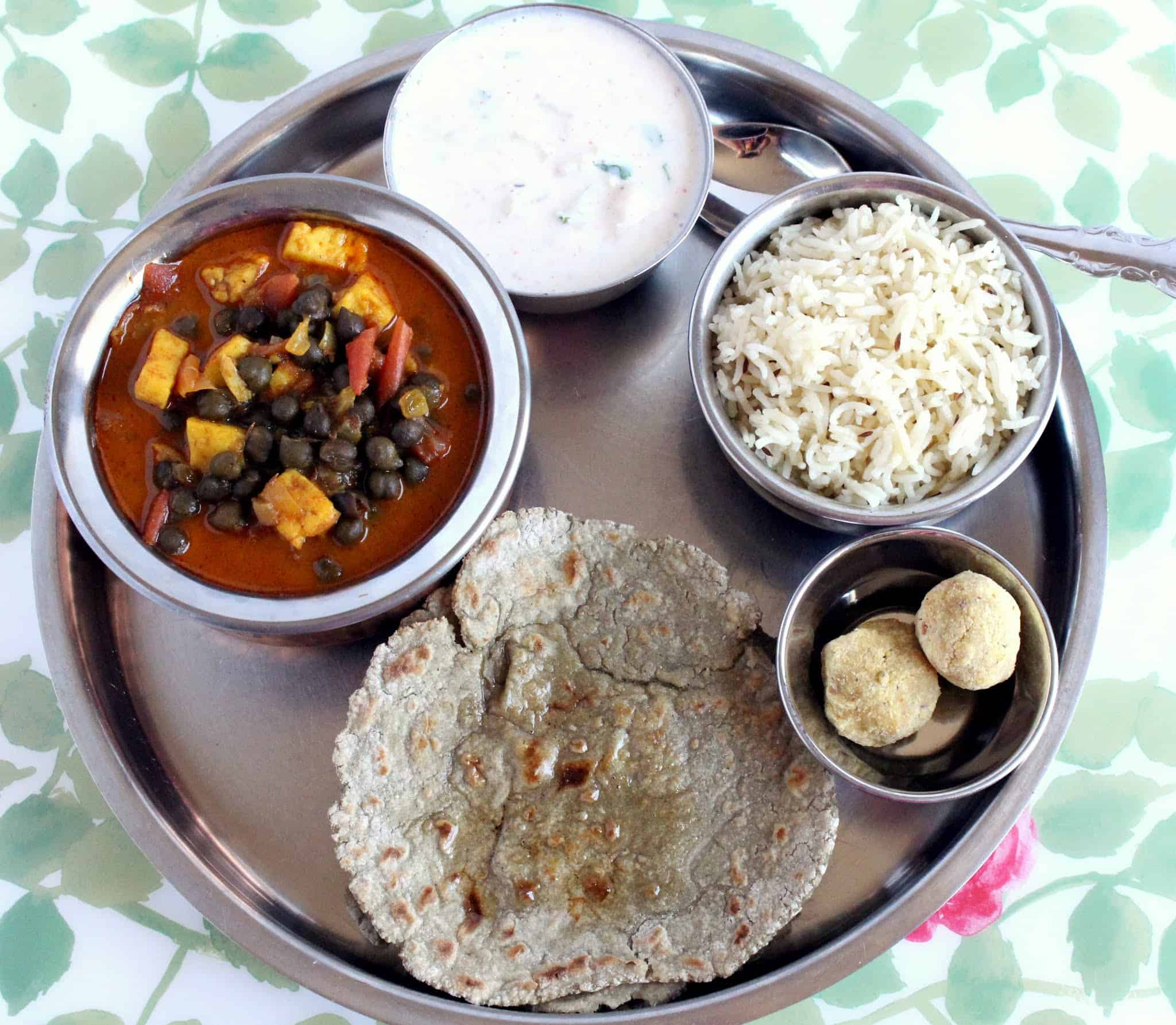 a plate with roti, curry, rice, raita and ladoo