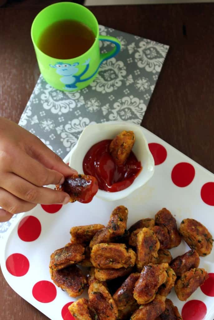 dipping baked zucchini potato tots inside ketchup