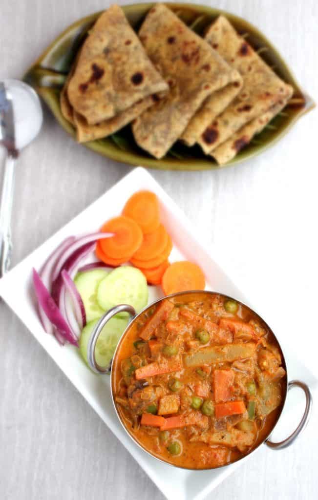 Kadai Vegetable Gravy with cucumber, tomato, Onion and carrot  in a white plate with Roti on the side
