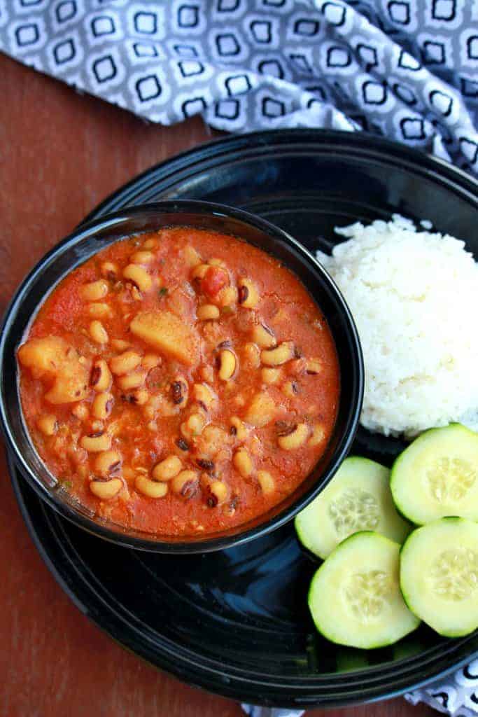 Black eyed peas and potato stew in a bowl with rice and cucumber on the side