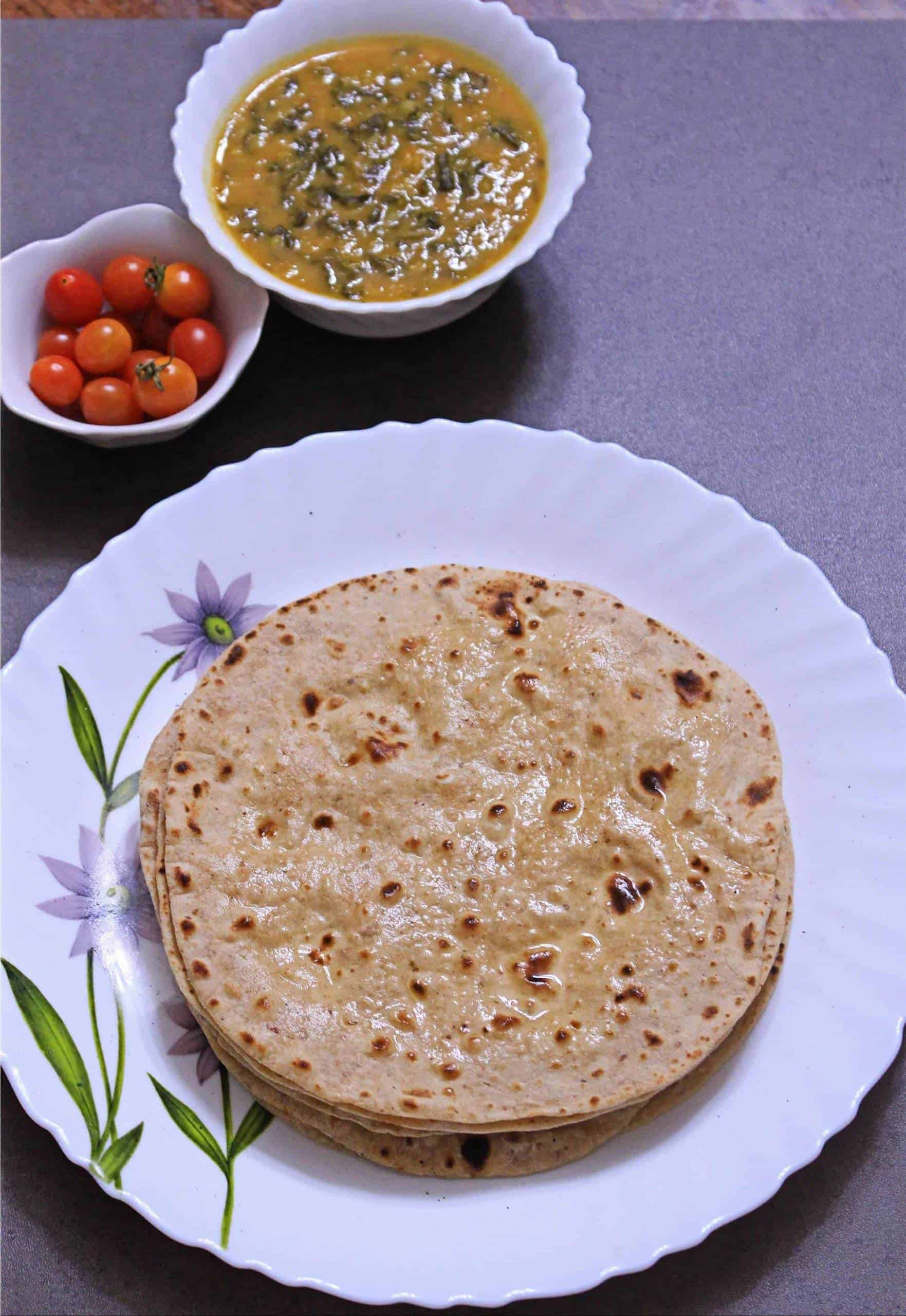 Whole Wheat Phulka in a white plate with subzi and tomatoes on the side.