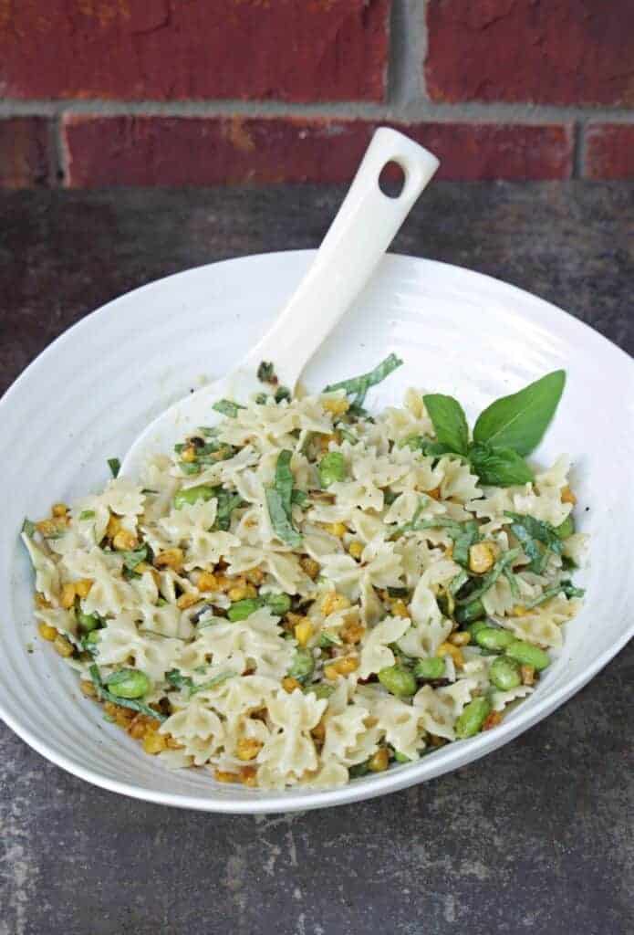 Pasta salad with roasted corn, edamame, spring onion and basil in a white bowl with white ladle