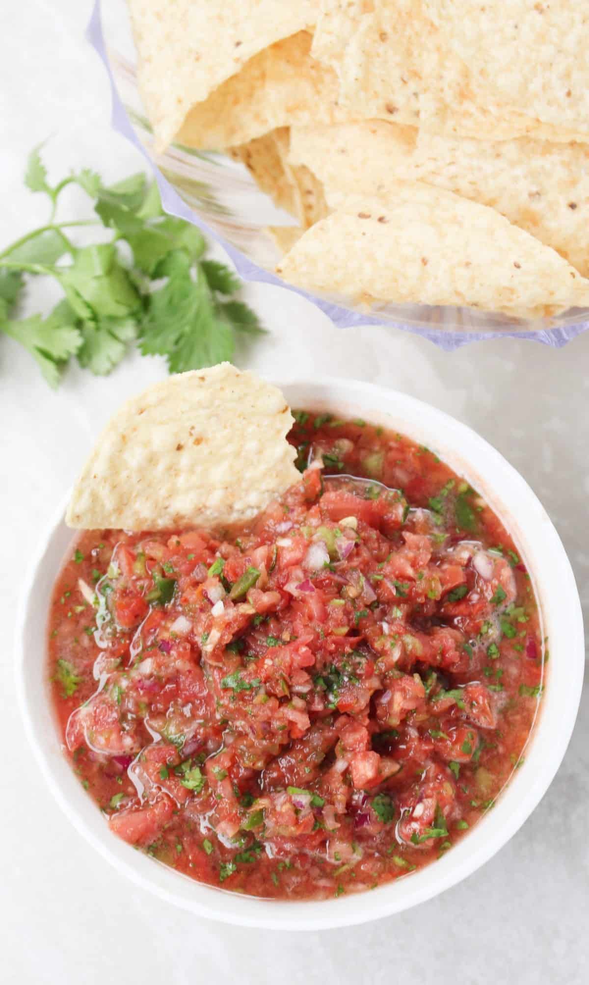 corn chips dipped into tomato salsa in a white bowl