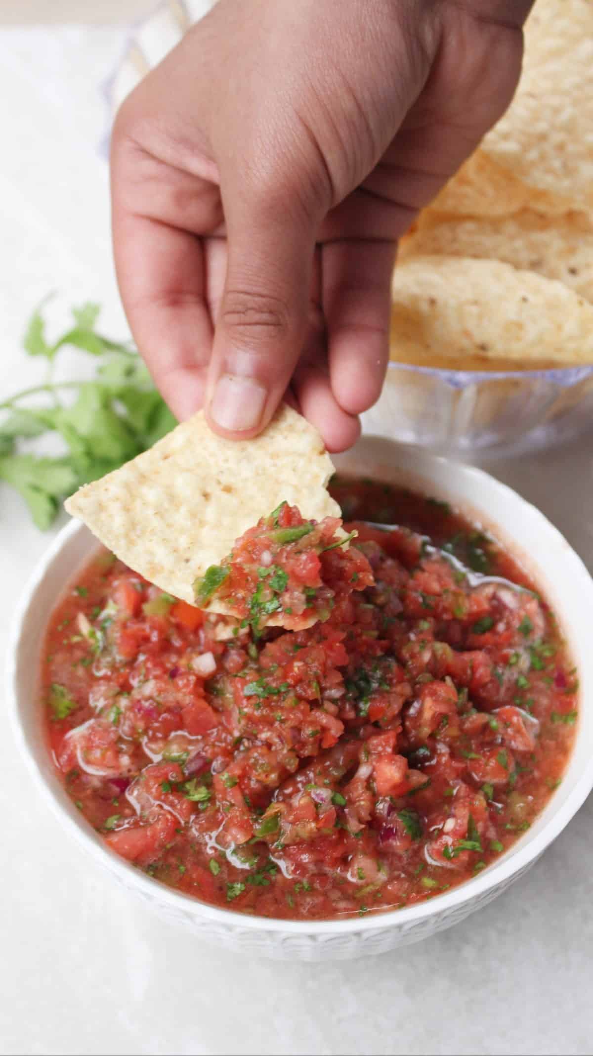 Tortilla chips scooping out tomato salsa from a white bowl