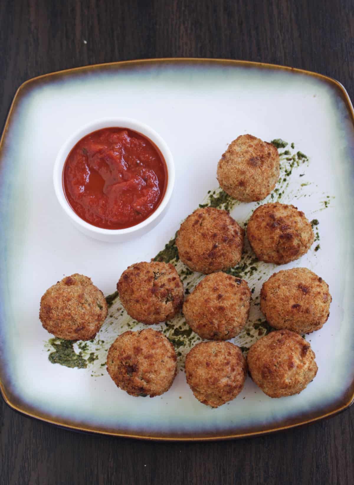 air fried Italian rice balls arranged in a plate with marinara sauce in bowl
