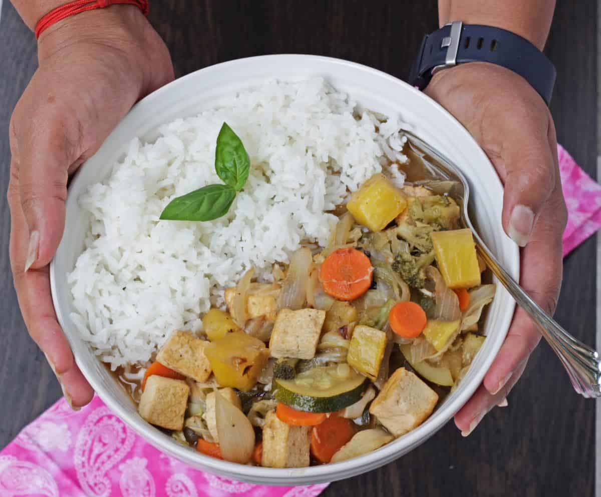 sweet and sour vegetables and tofu with rice in a bowl held in hand